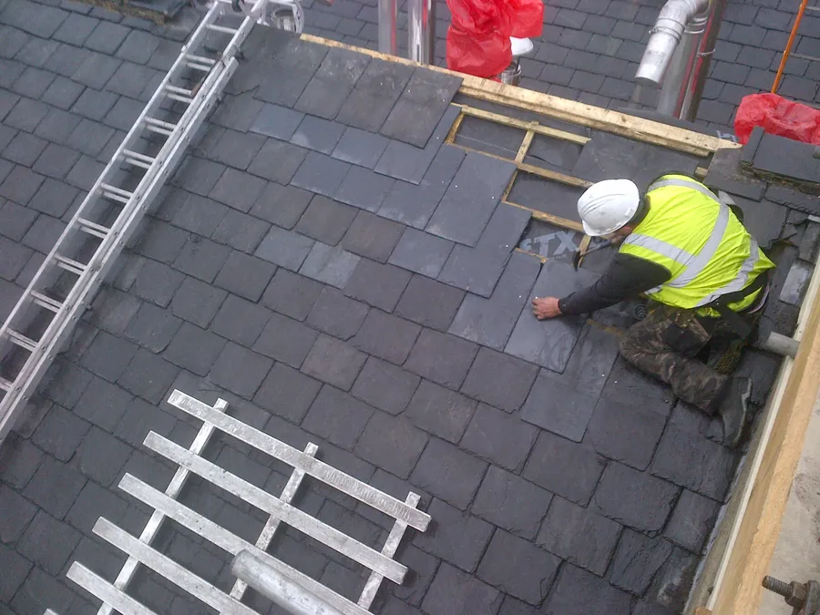 Roofer in a hard hat and hi-vis fixing new slates on a pitched roof