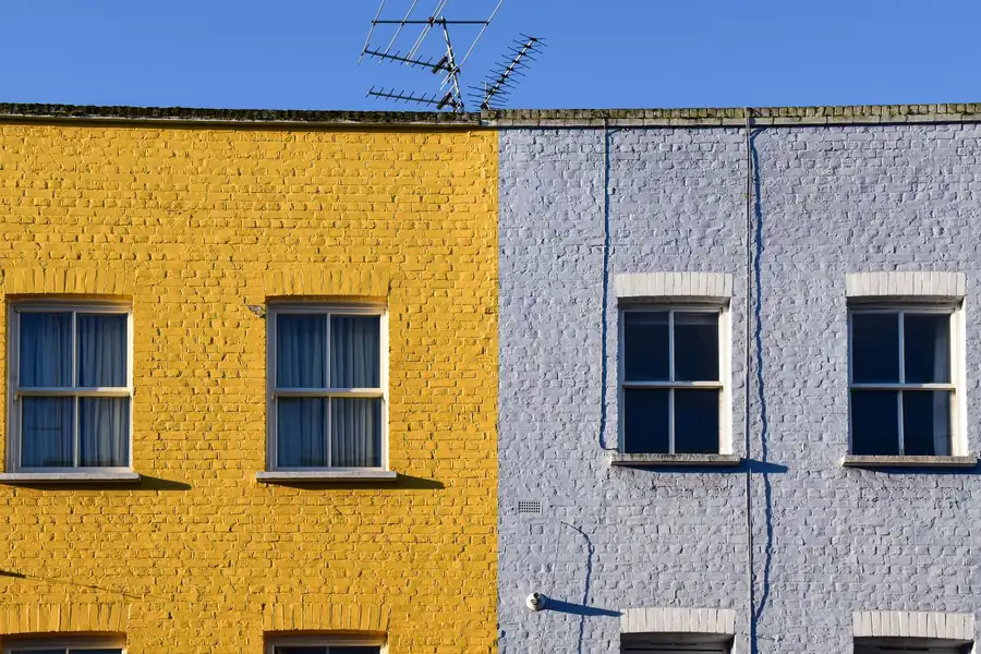 Two painted brick terraced houses, one yellow and one pale blue, with downpipes on the front walls